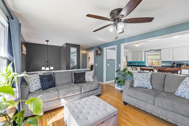 living area featuring baseboards, light wood-style floors, and ceiling fan with notable chandelier