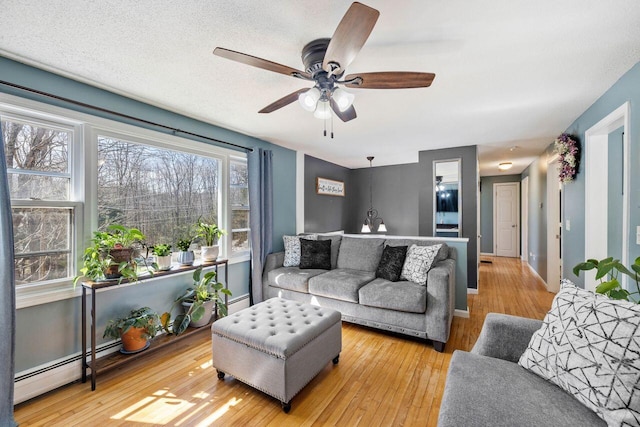 living area with a baseboard heating unit, hardwood / wood-style floors, a ceiling fan, and baseboards