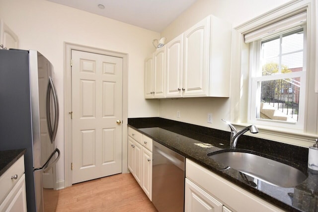 kitchen with appliances with stainless steel finishes, dark stone countertops, a sink, and light wood finished floors