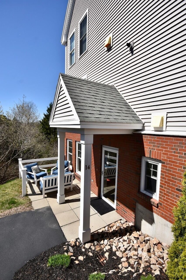 exterior space featuring an outdoor living space, brick siding, roof with shingles, and a patio