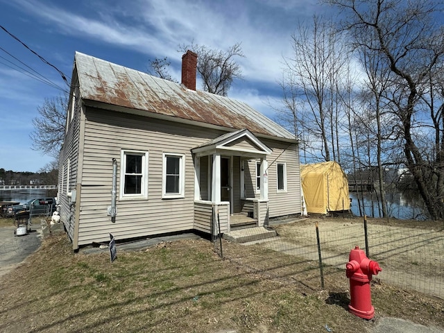 back of property featuring a chimney, metal roof, a standing seam roof, and fence