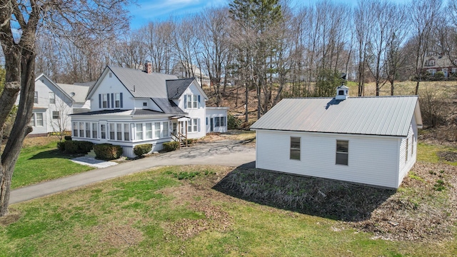 view of property exterior with a yard, a chimney, a sunroom, and metal roof