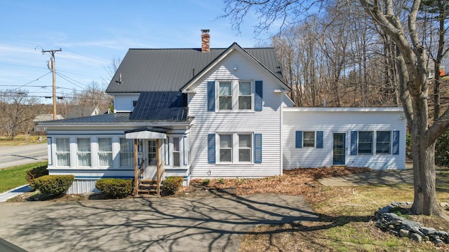 view of front facade featuring a chimney, metal roof, and a sunroom