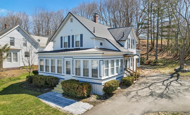 back of house featuring entry steps, a chimney, metal roof, and a sunroom