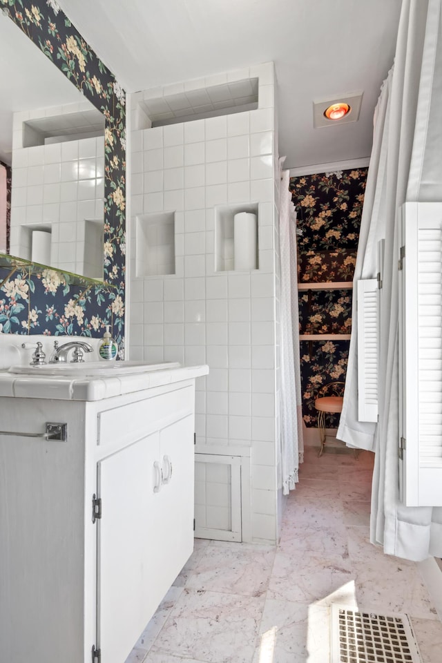 full bath featuring vanity, wallpapered walls, and marble finish floor