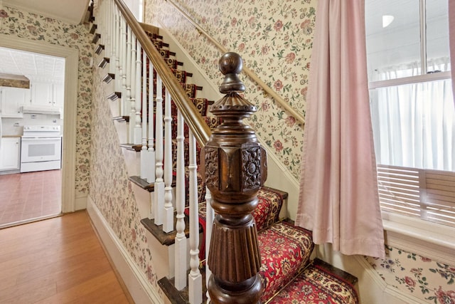 stairway featuring crown molding, wallpapered walls, and wood finished floors