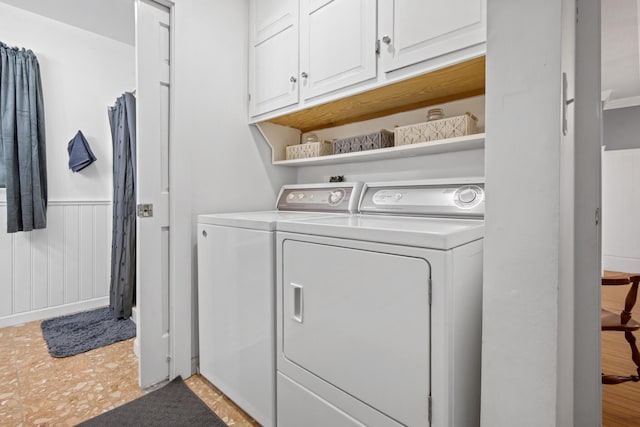 clothes washing area featuring cabinet space, separate washer and dryer, and a wainscoted wall