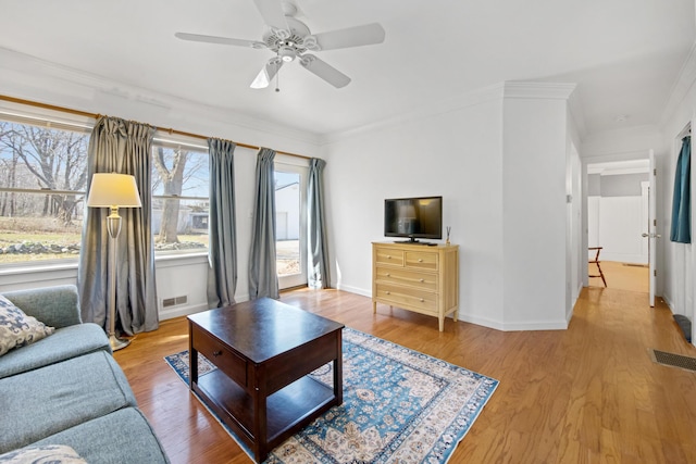 living area with ornamental molding, a ceiling fan, wood finished floors, and visible vents
