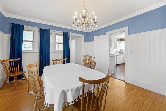 dining area with crown molding, wainscoting, light wood finished floors, a notable chandelier, and a decorative wall