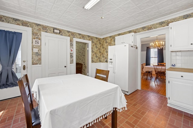dining space featuring brick patterned floor, an ornate ceiling, a chandelier, and a wainscoted wall