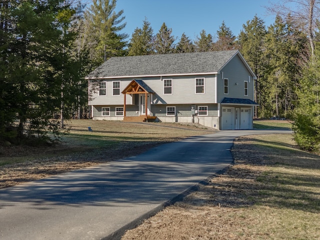 bi-level home featuring an attached garage, a front lawn, and aphalt driveway