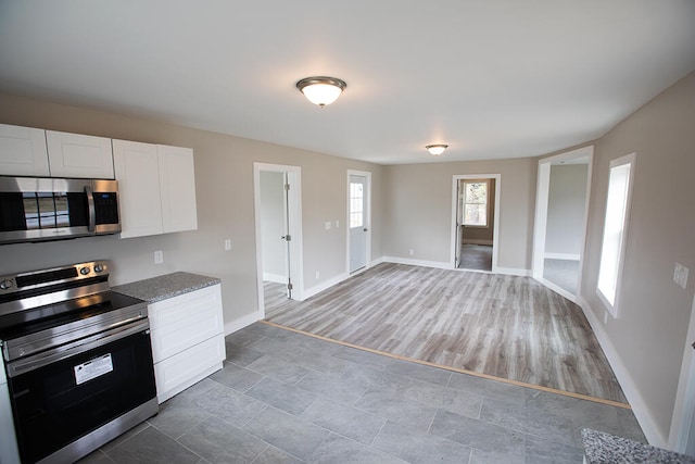 179 Main St, Corinth, ME 04427 - kitchen featuring stainless steel appliances, wood finished floors, baseboards, open floor plan, and white cabinetry