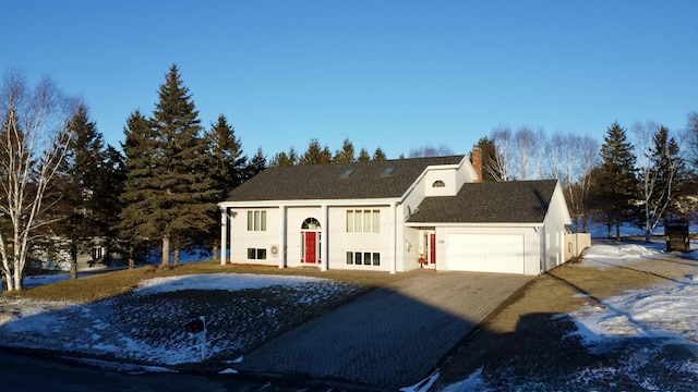 bi-level home with a chimney, driveway, a garage, stucco siding, and roof with shingles