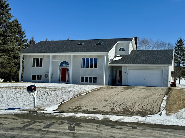 raised ranch with an attached garage, roof with shingles, and driveway