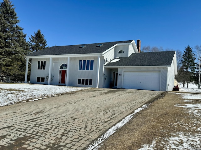 bi-level home with a chimney, an attached garage, and driveway
