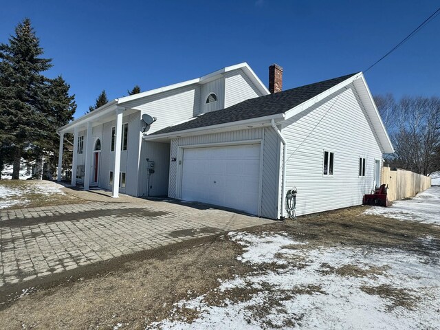 view of snow covered exterior featuring a chimney, driveway, fence, a garage, and roof with shingles