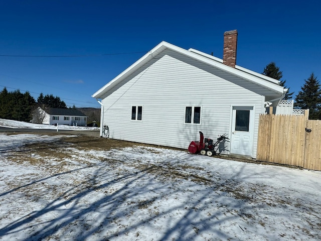 snow covered property featuring a chimney and fence