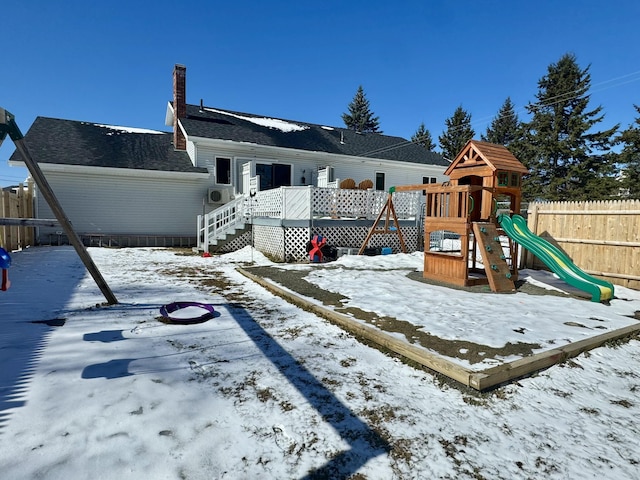 snow covered playground with fence, a deck, and a playground