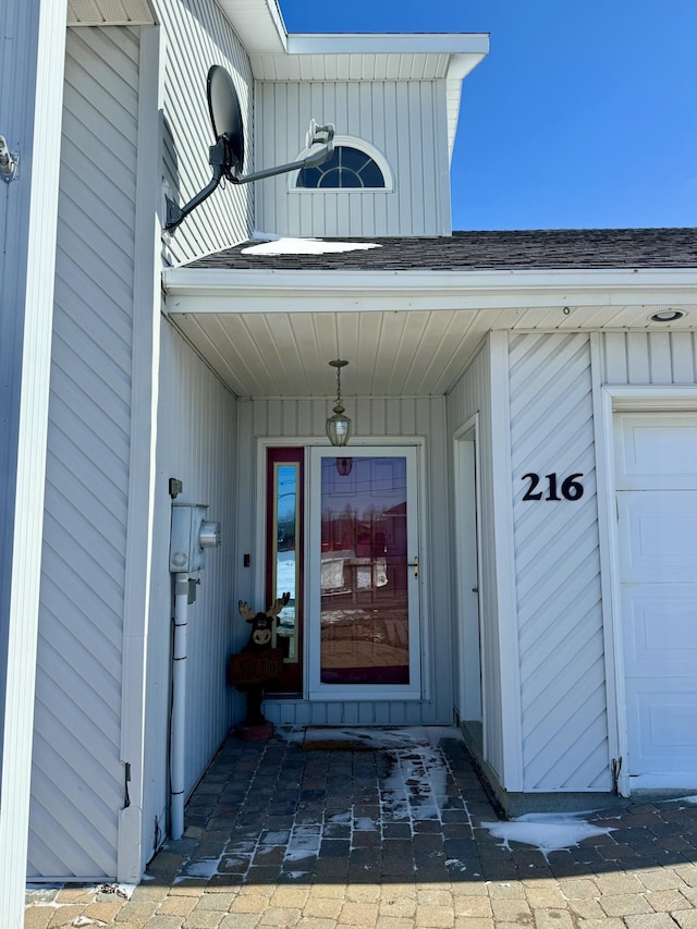 view of exterior entry featuring board and batten siding and a shingled roof