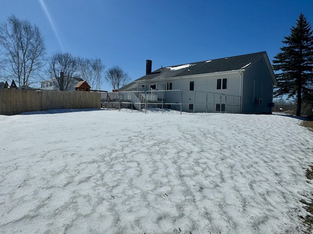 snow covered property featuring a chimney and fence