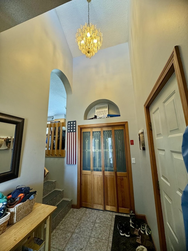 foyer entrance with high vaulted ceiling, stairs, arched walkways, an inviting chandelier, and baseboards
