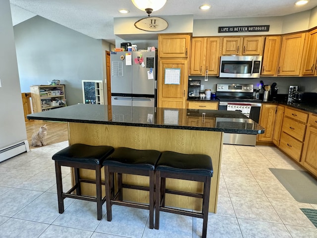 kitchen with light tile patterned flooring, a kitchen island, appliances with stainless steel finishes, and a kitchen breakfast bar