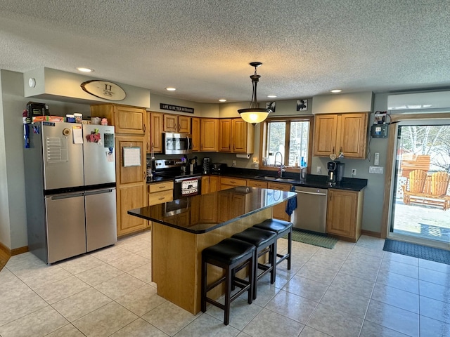 kitchen with brown cabinets, stainless steel appliances, dark countertops, a sink, and baseboards