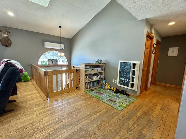 interior space with recessed lighting, wood finished floors, a wall unit AC, lofted ceiling with skylight, and a textured ceiling