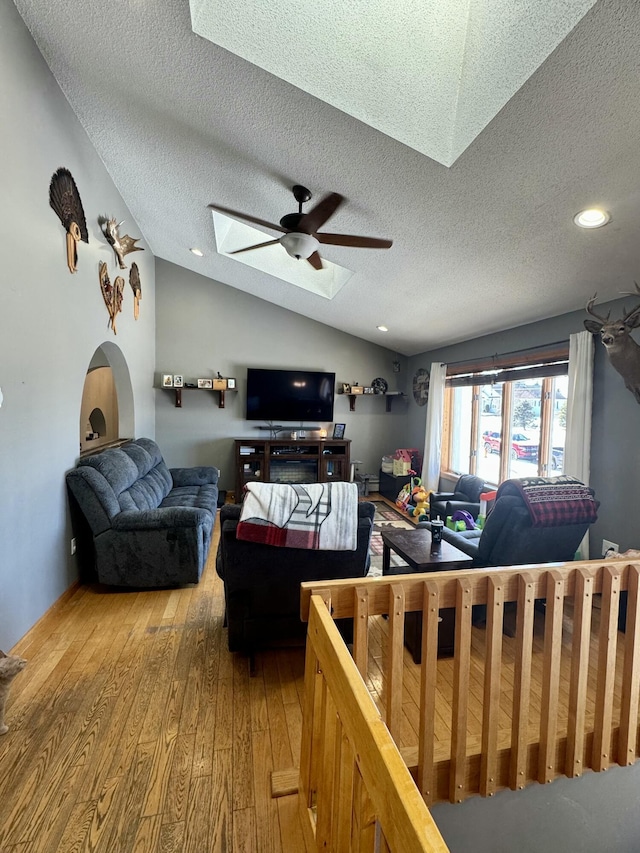 living room featuring lofted ceiling with skylight, a ceiling fan, a textured ceiling, and light wood finished floors