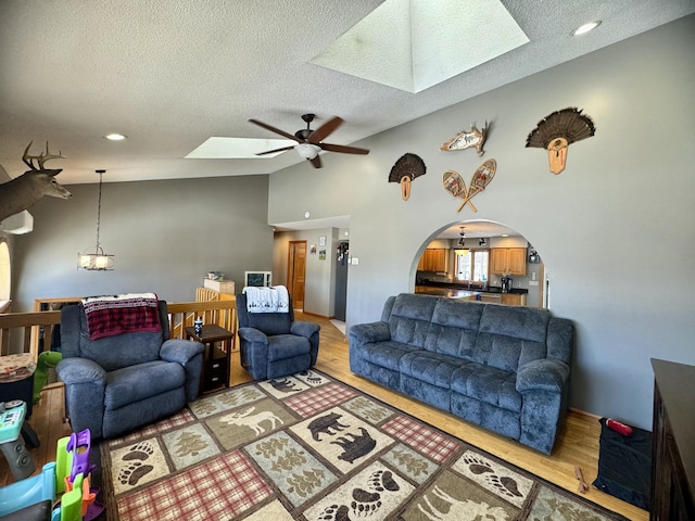 living area featuring vaulted ceiling with skylight, light wood-style flooring, a textured ceiling, and a ceiling fan