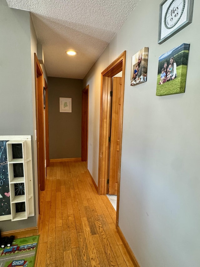 hall featuring wood-type flooring, a textured ceiling, and baseboards