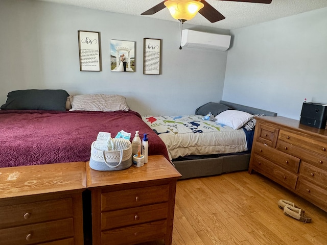 bedroom featuring light wood finished floors, a ceiling fan, an AC wall unit, and a textured ceiling