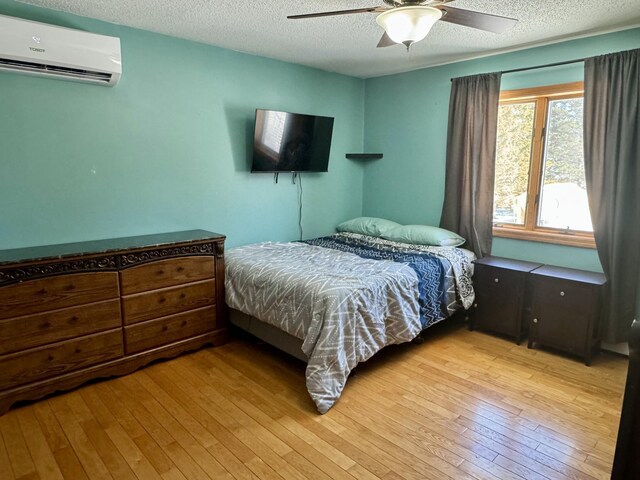bedroom with light wood-type flooring, a textured ceiling, a wall unit AC, and ceiling fan