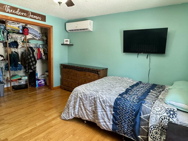 bedroom with wood finished floors, a wall unit AC, a closet, a textured ceiling, and ceiling fan