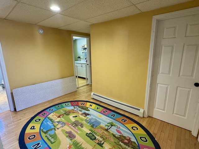 interior space featuring light wood-style floors, a drop ceiling, and baseboard heating
