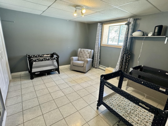 bedroom featuring a baseboard heating unit, baseboards, a paneled ceiling, and light tile patterned floors