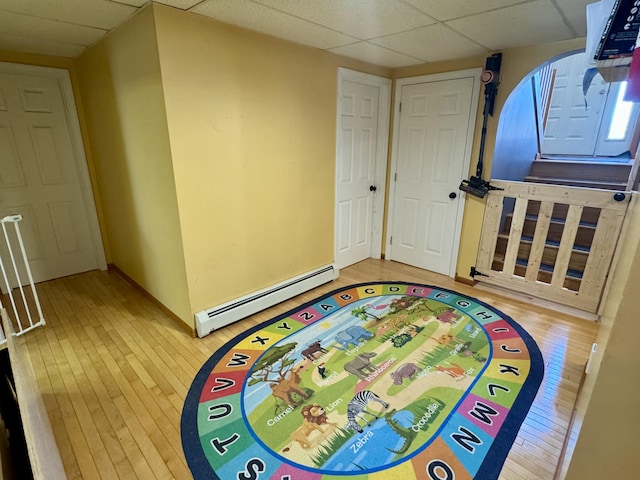 game room with a baseboard radiator, hardwood / wood-style floors, a drop ceiling, and baseboards