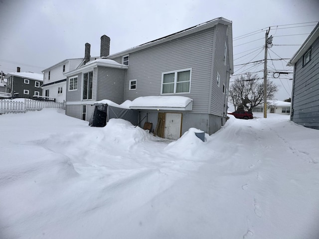 snow covered house with fence and a chimney