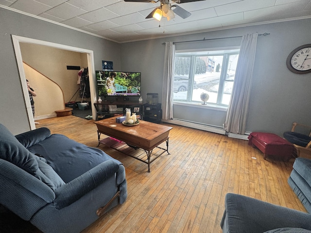 living area featuring a baseboard heating unit, a ceiling fan, ornamental molding, and wood-type flooring