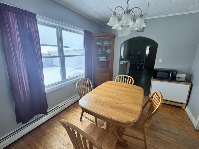 dining room with ornamental molding, arched walkways, wood-type flooring, a chandelier, and baseboard heating