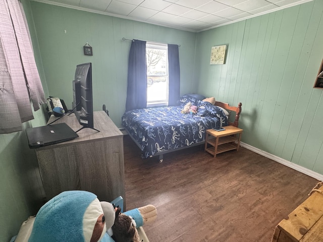 bedroom featuring wooden walls, wood finished floors, crown molding, and baseboards