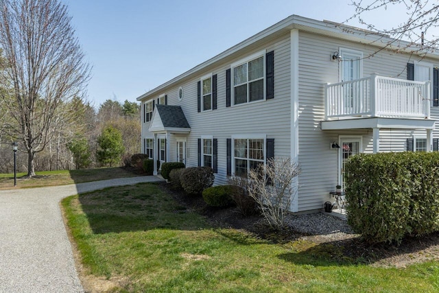 view of front facade with driveway, a balcony, and a front lawn
