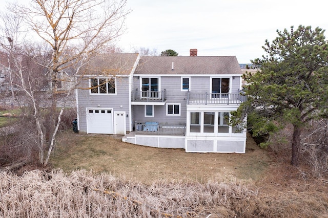 rear view of house with a balcony, a chimney, a lawn, an attached garage, and a patio