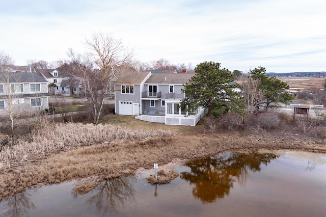 back of house with a chimney, an attached garage, a water view, and a balcony
