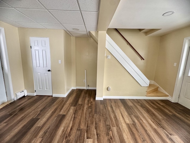 basement with a baseboard heating unit, a drop ceiling, baseboards, wood finished floors, and stairs