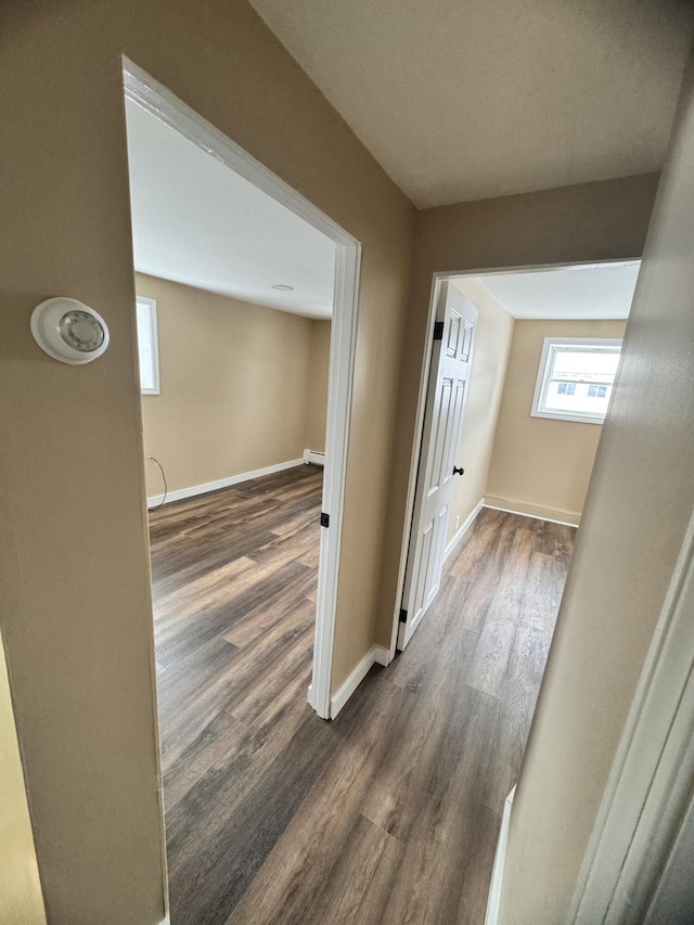 corridor with baseboards, a baseboard radiator, and dark wood-style flooring