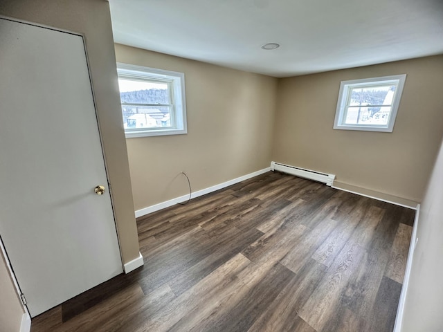 empty room featuring dark wood finished floors, a healthy amount of sunlight, and baseboard heating