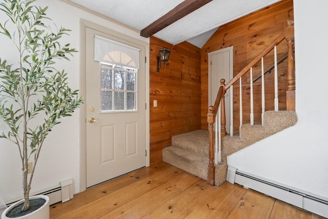 foyer featuring a baseboard heating unit, vaulted ceiling with beams, light wood-style floors, wood walls, and stairs
