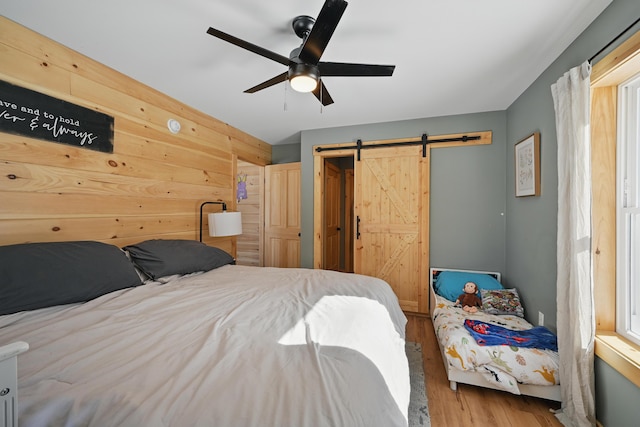 bedroom with wood walls, a ceiling fan, wood finished floors, and a barn door