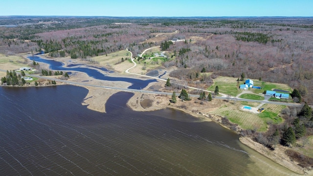 aerial view of property and surrounding area with a nearby body of water and a heavily wooded area